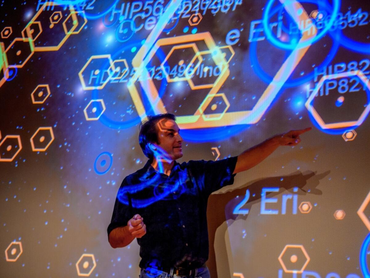 Man standing in front of projector screen, presenting a project to a group of people